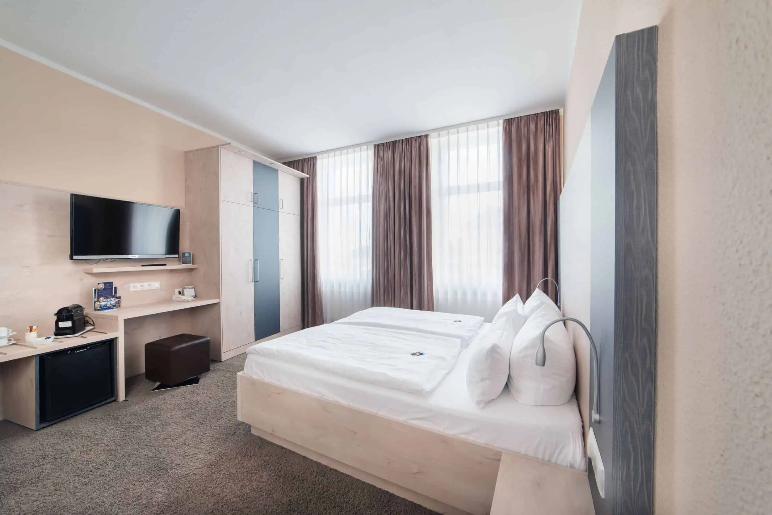 hotel-am-alten-strom-zimmer-interior-fotograf-008 Modern eingerichtetes Doppelzimmer im Hotel Am Alten Strom mit Schreibtisch, TV und bodentiefen Fenstern.