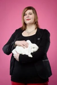 Frau in schwarzem Blazer hält ein weißes Kaninchen im Fotostudio vor pinkem Hintergrund.