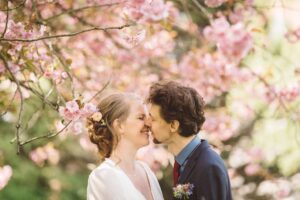 Romantischer Kuss des Brautpaares unter Kirschblüten in Rostock Brautpaar küsst sich liebevoll unter blühenden rosa Kirschblüten während eines Frühlingsshootings in Rostock.