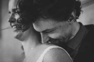 Innige Nähe und echtes Lachen – authentischer Hochzeitsmoment voller Liebe Emotionaler Moment eines Hochzeitspaares in Nahaufnahme – der Bräutigam lehnt liebevoll an der Schulter seiner Braut.