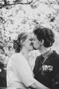 Martin Boerner Hochzeitspaar küsst sich zärtlich unter blühenden Kirschblüten – ein romantisches Schwarz-Weiß-Porträt voller Emotion.