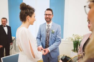 Ringtausch im Rostocker Standesamt – Hochzeitspaar beim emotionalen Versprechen Bräutigam im blauen Anzug steckt der Braut bei der standesamtlichen Trauung in Rostock einen Ring an – emotionaler Moment beim Ringtausch.