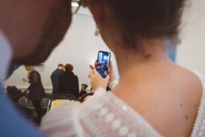 Digitale Nähe bei der Trauung – Videocall im Rostocker Standesamt Braut zeigt ein Smartphone mit Videotelefonie während der standesamtlichen Trauung im Rostocker Standesamt, auf dem eine ältere Frau liebevoll winkt.