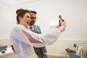 Brautpaar bei der Videotelefonie im Rostocker Standesamt – moderner Hochzeitsmoment Lachendes Brautpaar bei der Videotelefonie im Rostocker Standesamt – die Braut hält ein Smartphone für einen Anruf in die Kamera.