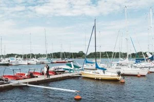 Hochzeitsfoto am Stadthafen in Rostock mit Segelbooten Ein frisch verheiratetes Paar steht auf einem Steg im Stadthafen von Rostock und küsst sich liebevoll, umgeben von weißen Segelbooten, Motorbooten und blauem Himmel – eine romantische Szene mit maritimem Flair.
