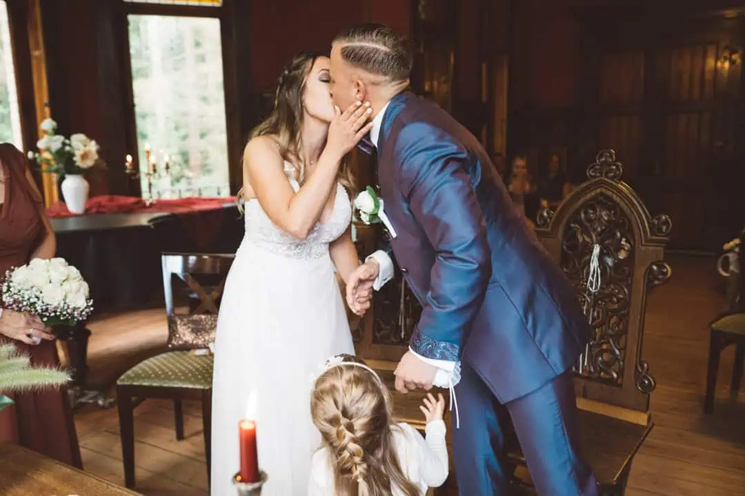 Hochzeitskuss des Brautpaares während der Trauung im Jagdschloss Gelbensande, kleines Mädchen greift nach ihrer Hand.