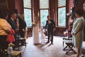 Brautpaar mit Tochter bei der standesamtlichen Trauung im Jagdschloss Gelbensande, umgeben von Gästen.