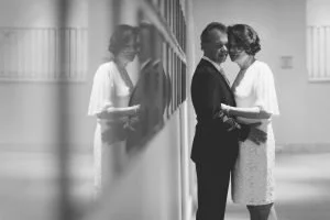 Ein elegantes Brautpaar steht eng umschlungen an einer spiegelnden Wand im Grand Hotel Heiligendamm, festlich gekleidet in Anzug und Spitzenkleid – künstlerische Hochzeitsfotografie in Schwarz-Weiß mit emotionaler Tiefe.