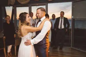 Braut und Bräutigam tanzen ihren Eröffnungstanz bei Sonnenuntergang in Markgrafenheide, umgeben von Gästen.