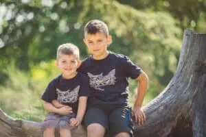 Zwei Brüder im Botanischen Garten Rostock, die auf einem Baumstumpf sitzen und zusammen lächeln.