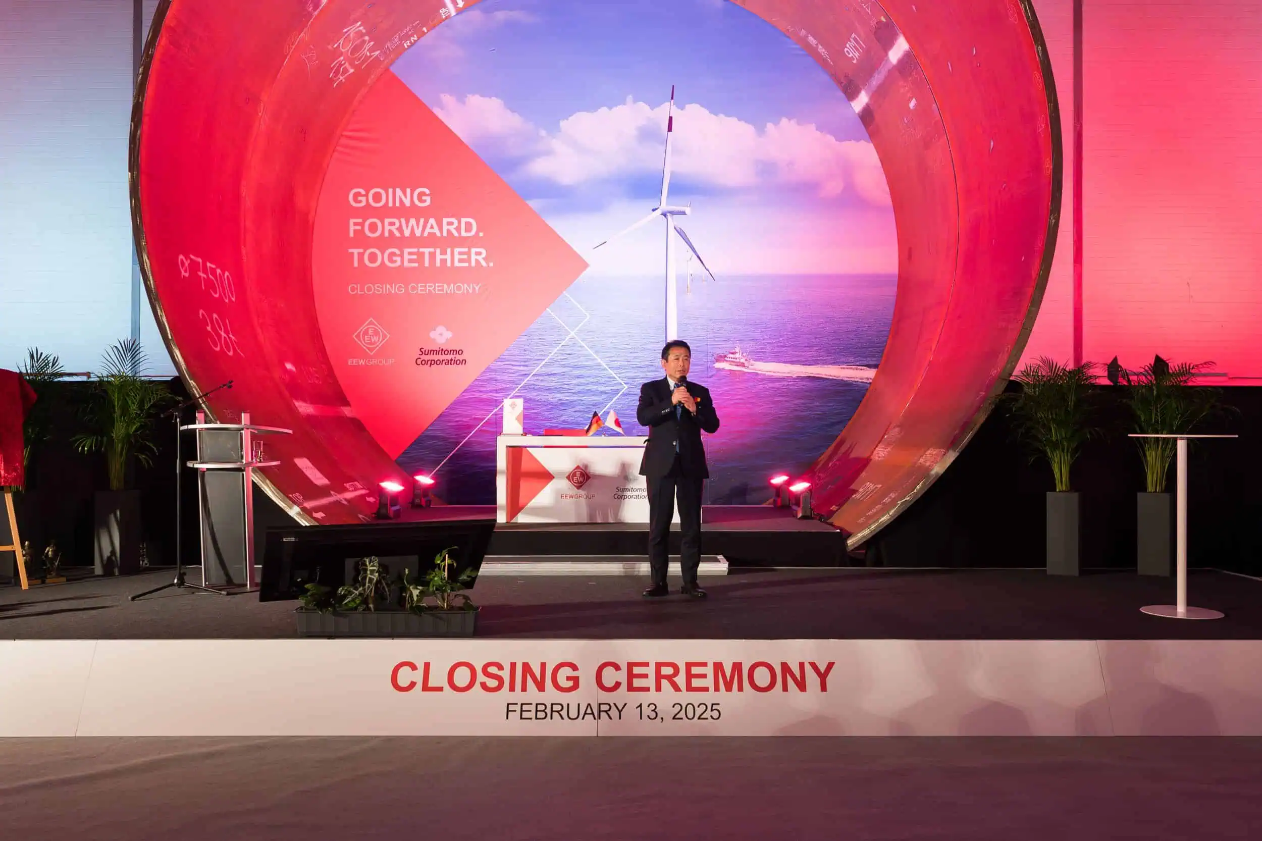 business-event-fotograf-eew-rostock-196 Redner bei der Closing Ceremony von EEW und Sumitomo Corporation am 13. Februar 2025 vor großem Offshore-Windkraft-Motiv.