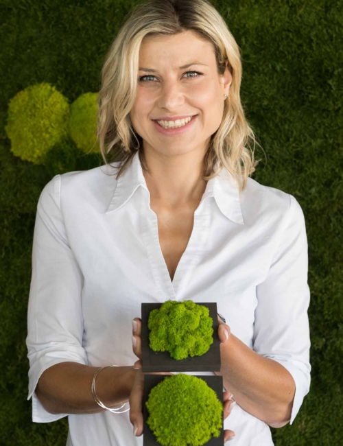 Moos Antje Gude hält zwei Moosproben in der Hand vor einer grünen Mooswand.