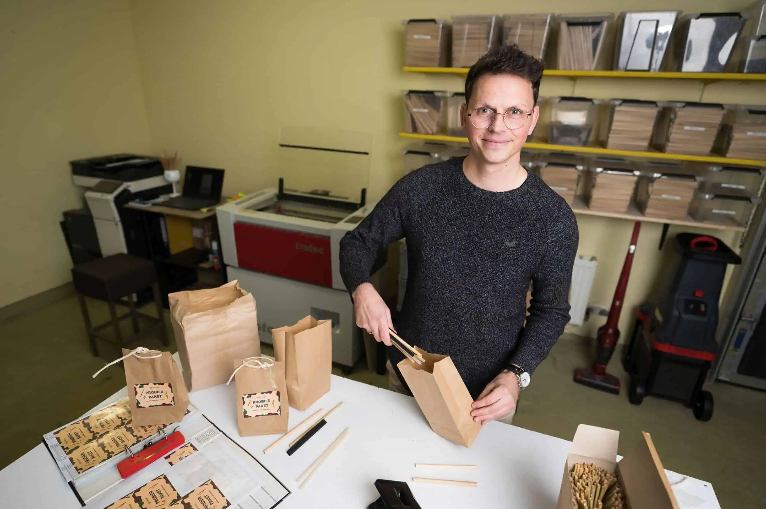 Rohalm Phillip Stein von Rohalm verpackt nachhaltige Trinkhalme in Papierbeutel an einem weißem Tisch in der Werkstatt.