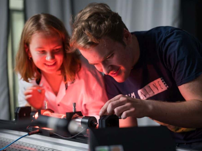 Zwei Studenten der physikalischen Fakultät der Uni Rostock bei einem Versuchsaufbau Ein Mitarbeiter und eine Mitarbeiterin der Uni Rostock arbeiten freudig an einer Maschine.