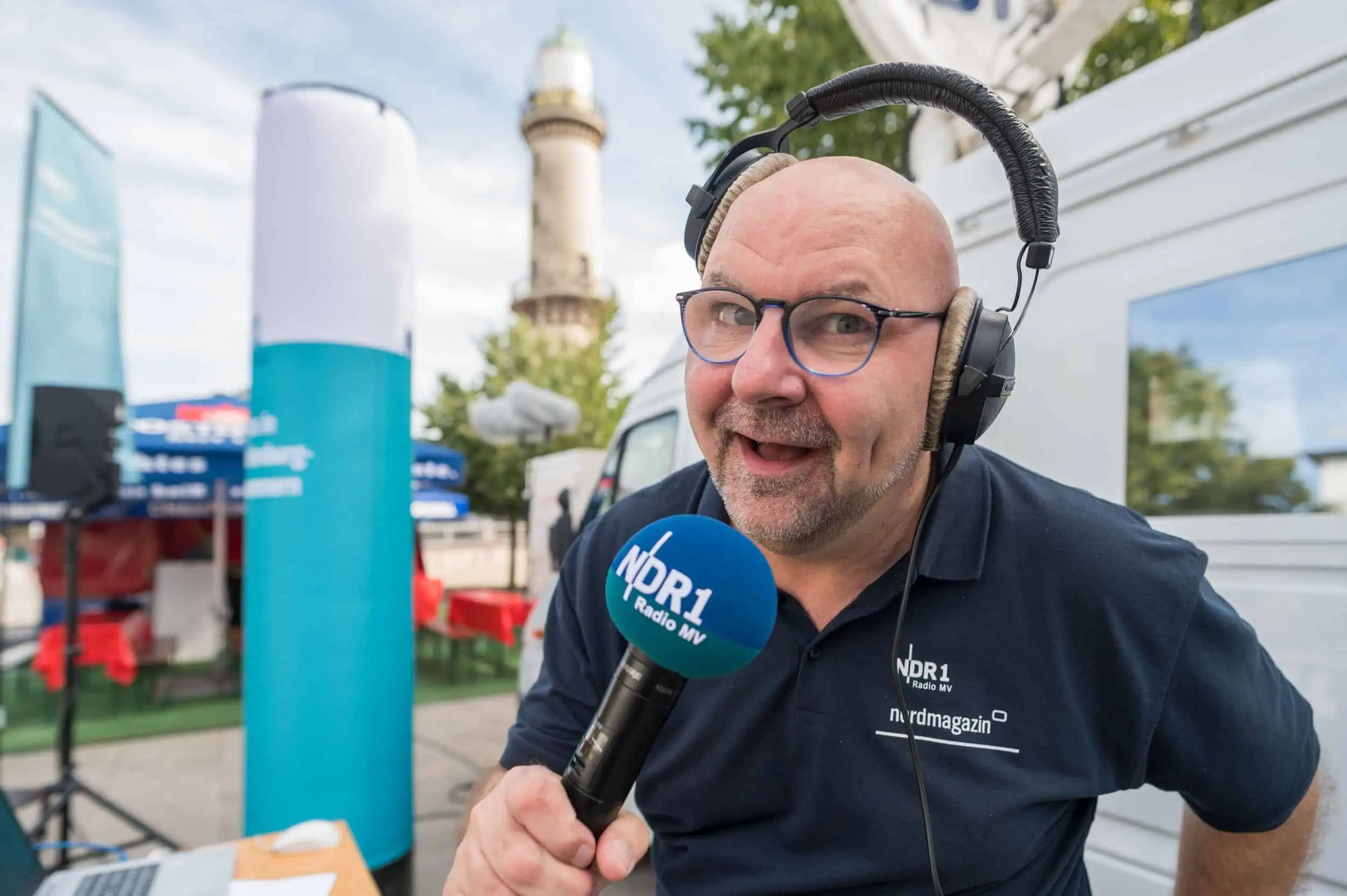 Martin Boerner Marc Angerstein vom NDR mit Headset und Mikrofon bei Außenmoderation vor dem Leuchtturm Warnemünde.