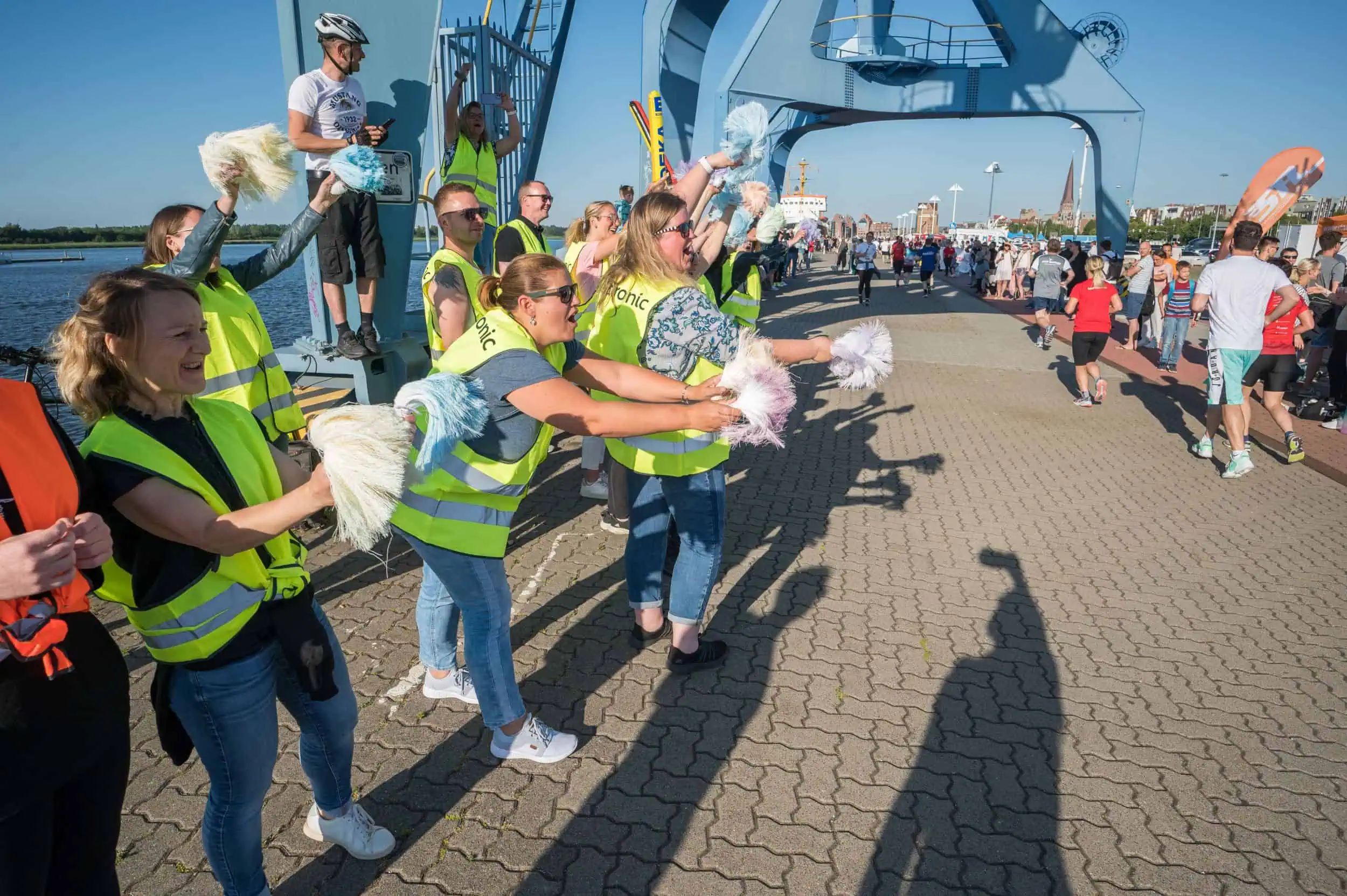 Martin Boerner Fans in Warnwesten feuern Teilnehmende des Rostocker Citylaufs mit Pompons an einer Brücke lautstark an.