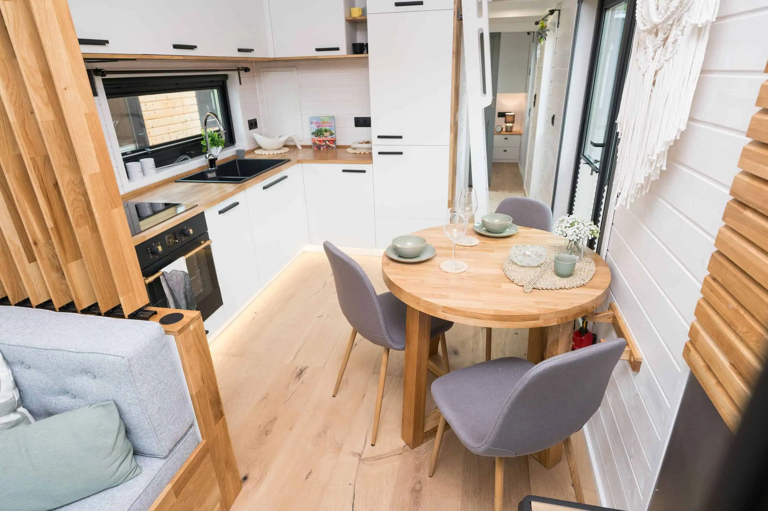 So lebt es sich im Tiny House Moderne Küche mit Essbereich in einem Tiny House von Mobi House in Bentwisch, ausgestattet mit weißer Einbauküche, rundem Holztisch und stilvollen Details.