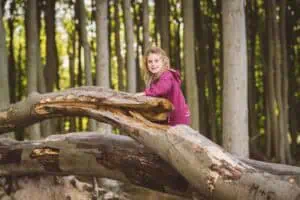 Mädchen mit blonden Locken in pinker Jacke klettert auf einem dicken Baumstamm im Gespensterwald Nienhagen.
