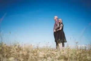 Tattoo-Paar umarmt sich liebevoll in den Dünen von Ahrenshoop vor strahlend blauem Himmel – modernes und natürliches Paarshooting an der Ostsee.