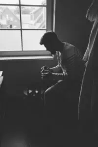 Bräutigam sitzt im Halbdunkel eines Zimmers am Fenster und bereitet sich auf die Hochzeit vor – nachdenklicher Moment beim Getting Ready.