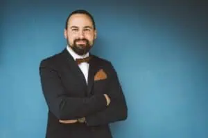 Porträt eines Bräutigams im eleganten dunklen Anzug mit Fliege und Einstecktuch, posierend vor einer blauen Wand am Tag der Hochzeit.