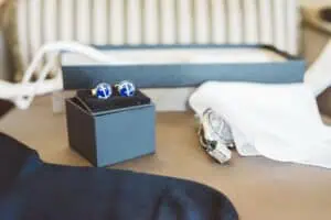 Nahaufnahme von maritimen Manschettenknöpfen mit Anker-Motiv, einer silbernen Armbanduhr und einem weißen Einstecktuch – stilvolle Hochzeitsaccessoires für den Bräutigam.