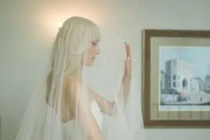 Seitliches Portrait einer Braut mit langem Schleier, die sich sanft den Tüll vors Gesicht legt, im Hintergrund