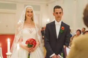 Brautpaar während der standesamtlichen Trauung im Grand Hotel Heiligendamm, Braut im weißen Kleid mit rotem Brautstrauß, Bräutigam im dunklen Anzug.