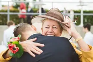 Emotionale Umarmung zwischen Hochzeitsgast mit Hut und Bräutigam beim Sektempfang in Heiligendamm.