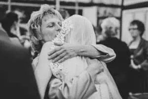 Emotionale Umarmung zwischen Braut und älterer Frau während einer Hochzeitsfeier, festgehalten in schwarz-weiß.