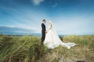 Brautpaar steht im hohen Dünengras am Ostseestrand von Heiligendamm, Hand in Hand, mit weitem Himmel und Meer im Hintergrund.