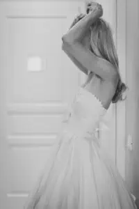 Schwarzweißaufnahme einer Braut beim Getting Ready im Hochzeitskleid mit Corsage im Grand Hotel Heiligendamm – sie richtet ihr Haar vor der Trauung.