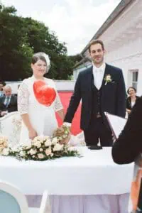 Brautpaar bei der Trauung im Grand Hotel Heiligendamm, mit rotem Herzballon, floraler Tischdekoration und einem Kind mit Blumenkranz, das sich über den Tisch beugt.