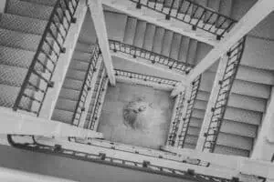 Aus der Vogelperspektive fotografierte Szene einer Braut in fließendem Kleid, die im quadratisch angelegten Treppenhaus des Grand Hotel Heiligendamm steht – kunstvolle Hochzeitsfotografie mit architektonischem Fokus in Schwarz-Weiß.