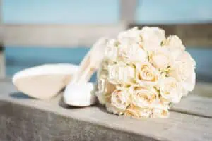 Cremefarbener Brautstrauß aus Rosen liegt neben eleganten weißen Brautschuhen auf einer Holzbank mit Blick auf die Ostsee in Heiligendamm.