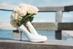 Weiße Brautschuhe mit einem cremefarbenen Rosenstrauß darin, arrangiert auf einer Holzbank an der Ostsee in Heiligendamm.