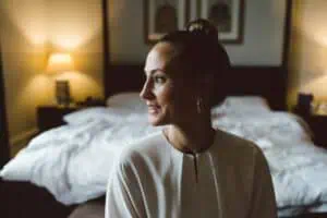 Braut sitzt lächelnd im Hotelzimmer auf dem Bett, seitlich beleuchtet vom warmen Licht einer Nachttischlampe im Grand Hotel Heiligendamm.