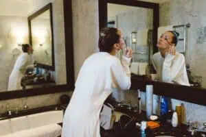 Braut trägt im Badezimmer des Grand Hotel Heiligendamm Mascara auf und schaut konzentriert in den Spiegel – Getting Ready Moment.