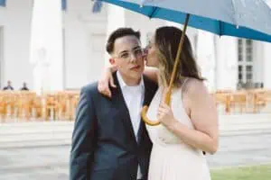 Junge Frau küsst einen Hochzeitsgast liebevoll auf die Wange unter einem blauen Regenschirm vor dem Grand Hotel Heiligendamm.