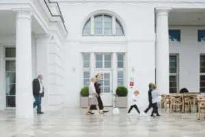 Hochzeitsgäste und spielende Kinder auf der eleganten Außenterrasse des Grand Hotel Heiligendamm mit klassizistischer Architektur im Hintergrund.