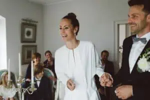 Braut und Bräutigam lächeln glücklich während der standesamtlichen Trauung im Grand Hotel Heiligendamm, umgeben von fröhlichen Gästen.