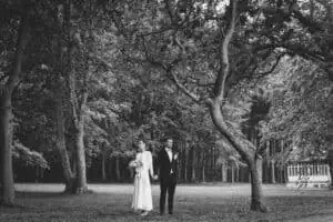 Braut und Bräutigam stehen Hand in Hand in einem bewaldeten Park beim Grand Hotel Heiligendamm, umgeben von alten Bäumen.