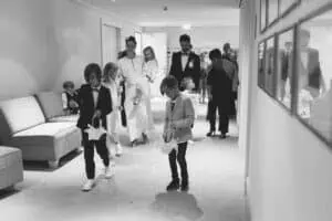 Hochzeitsgesellschaft im Grand Hotel Heiligendamm, darunter Kinder als Blumenkinder, die Blütenblätter im Flur streuen, begleitet von elegant gekleideten Erwachsenen.