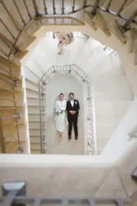 Braut und Bräutigam liegen nebeneinander im Treppenhaus des Grand Hotel Heiligendamm und blicken lächelnd nach oben in die Kamera.