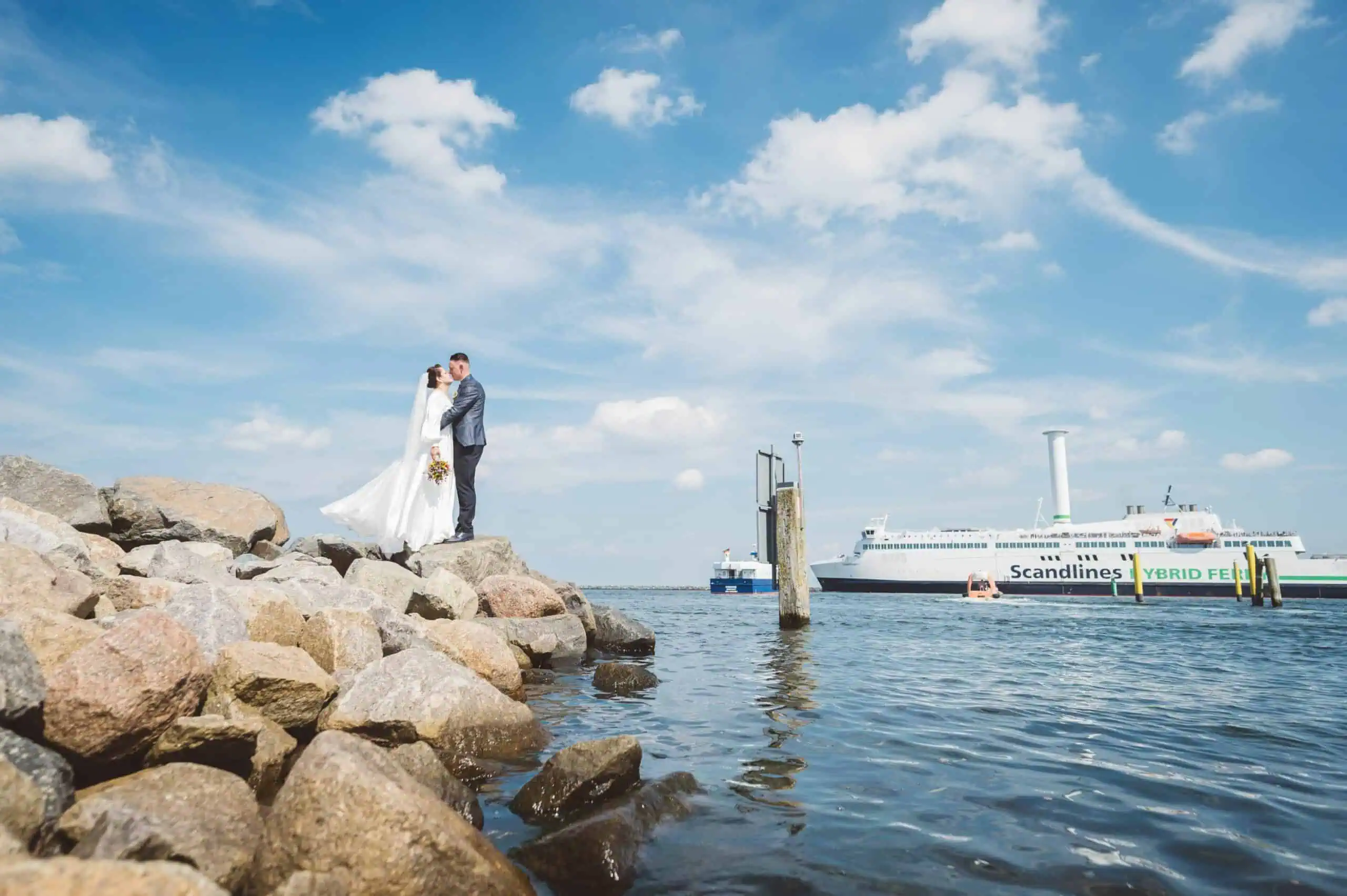 Hochzeits-Fotoshooting Paket Standesamt Brautpaar auf einer felsigen Küste bei sonnigem Himmel, im Hintergrund eine Fähre von Scandlines