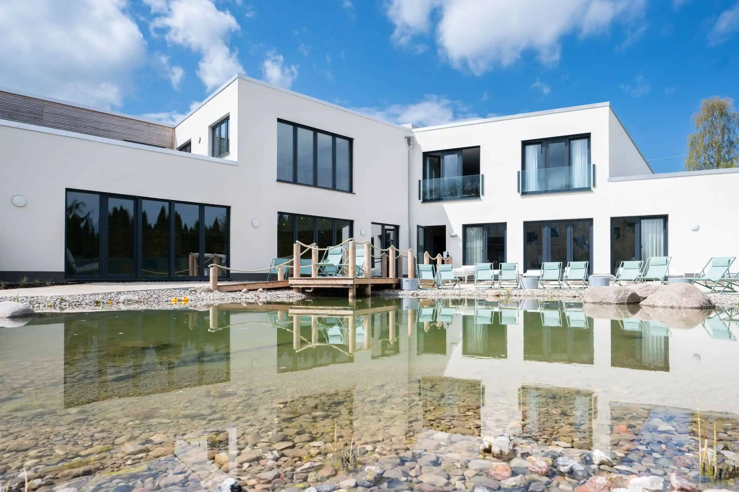 Ausbau Landhotel Rittmeister Außenansicht des Hotel Rittmeister in Biestow mit moderner Architektur, Sonnenliegen und Naturteich unter blauem Himmel.