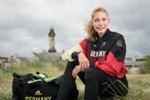 Lindy Ave, paralympische Athletin, in Sportkleidung mit "Germany"-Jacke in den Dünen von Warnemünde vor dem Leuchtturm.