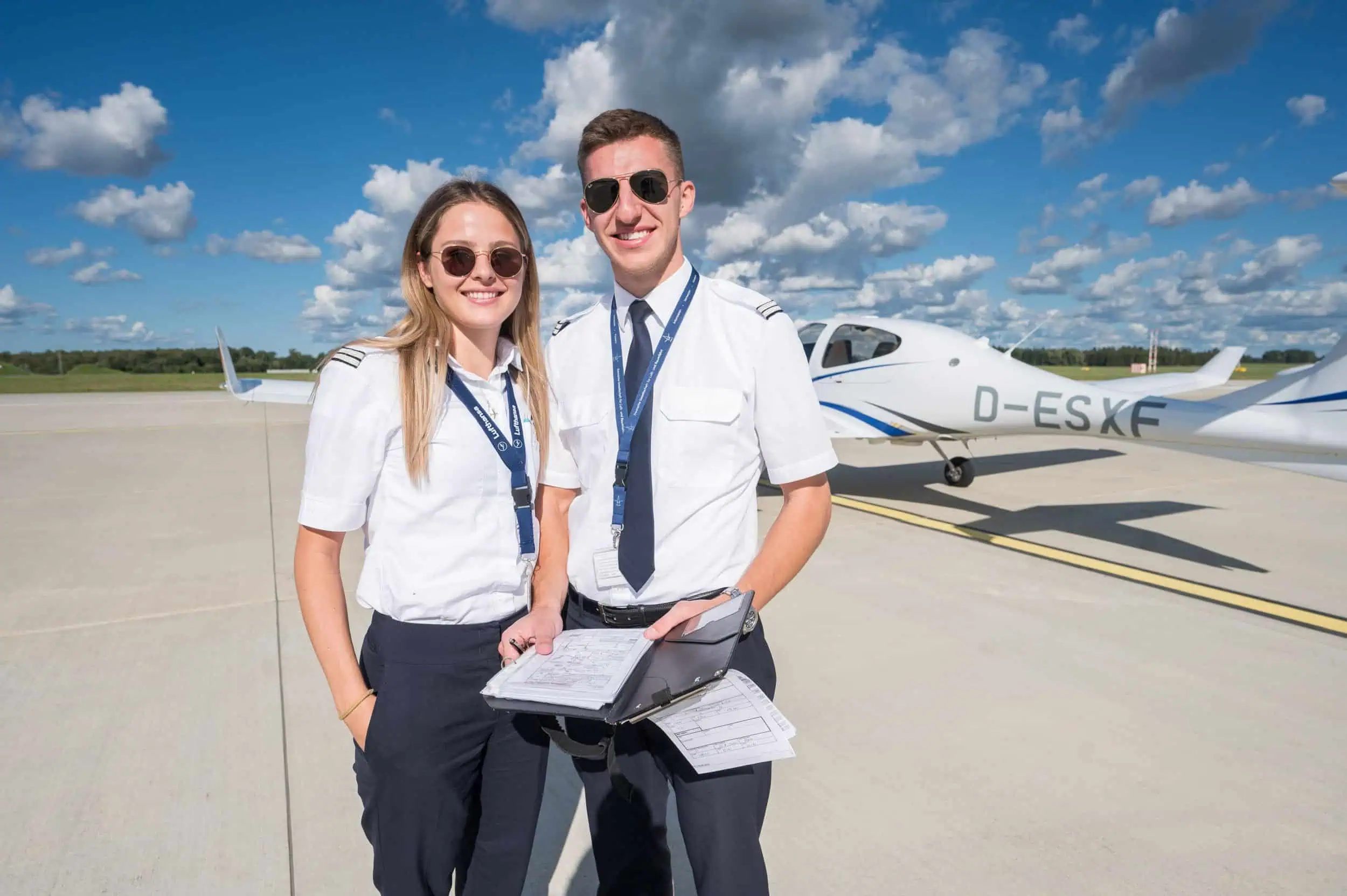 European Flight Academy Rostock Zwei Flugschüler, Tami Schumann (24) und Nils Ellenrieder (21) , in Pilotenuniform stehen mit Flugunterlagen vor einem Schulungsflugzeug der Lufthansa.