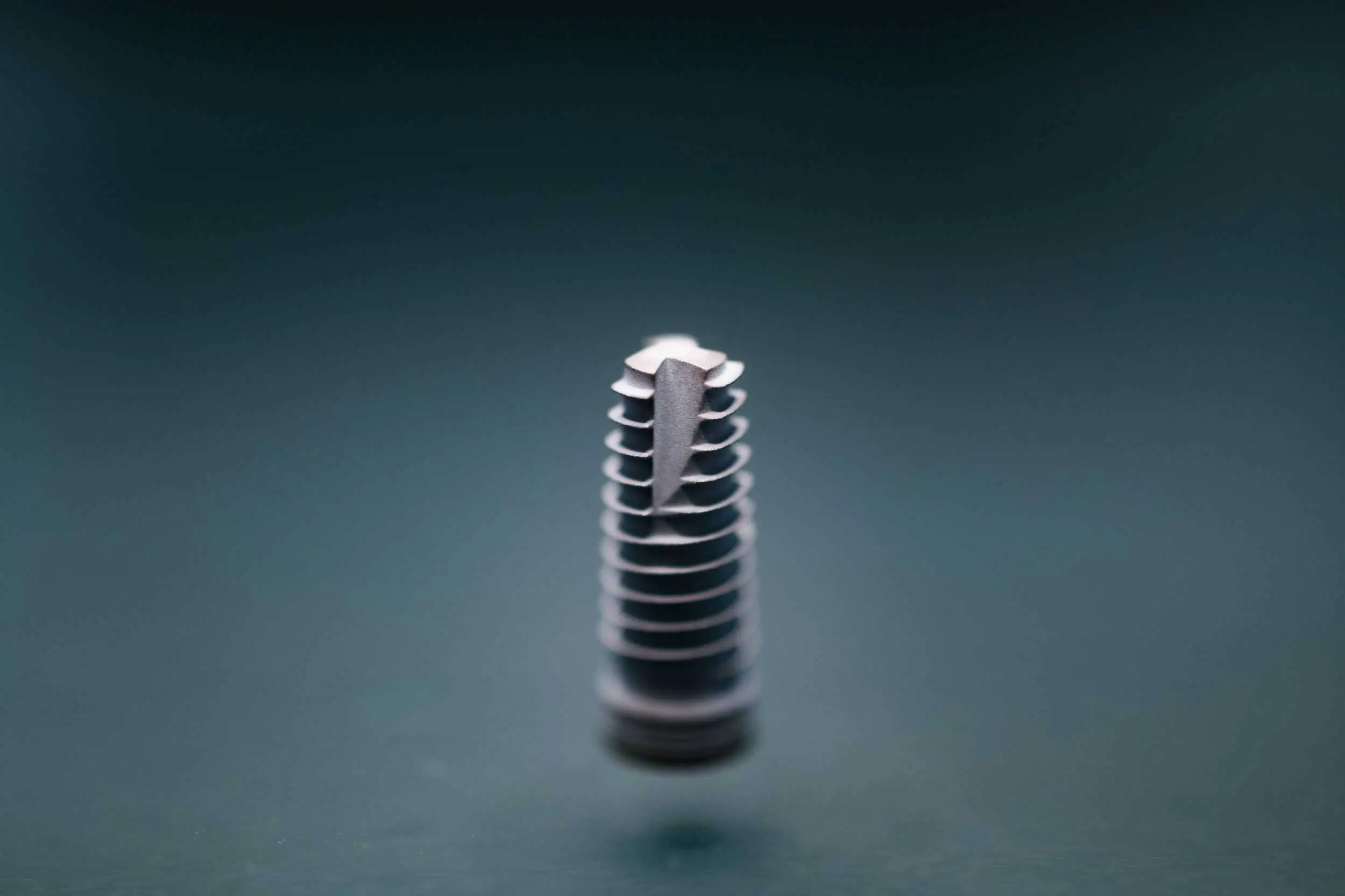 unternehmensfotos-fmz-business-foto-023 Detailaufnahme eines Dentalimplantats aus dem FMZ – präzise gefertigte Titanstruktur mit Schraubgewinde zur Verankerung im Kieferknochen.