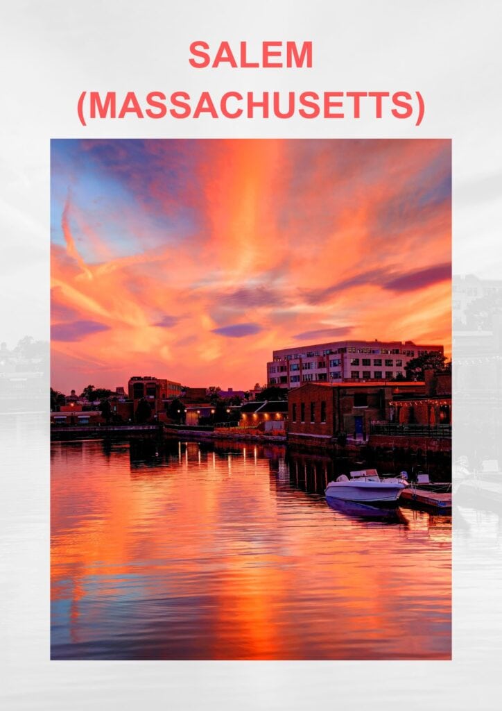 The waterfront of Salem, Massachusetts, under a dramatic sky. The sunset reflects vibrant oranges and pinks in the calm water, with boats moored along the dock and the city's buildings illuminated by the warm glow.